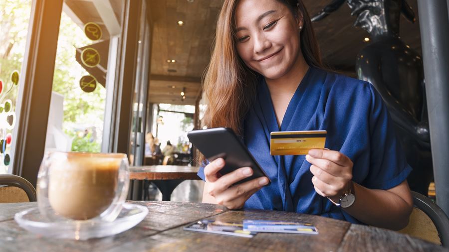 Woman using phone while holding card in a coffee shop