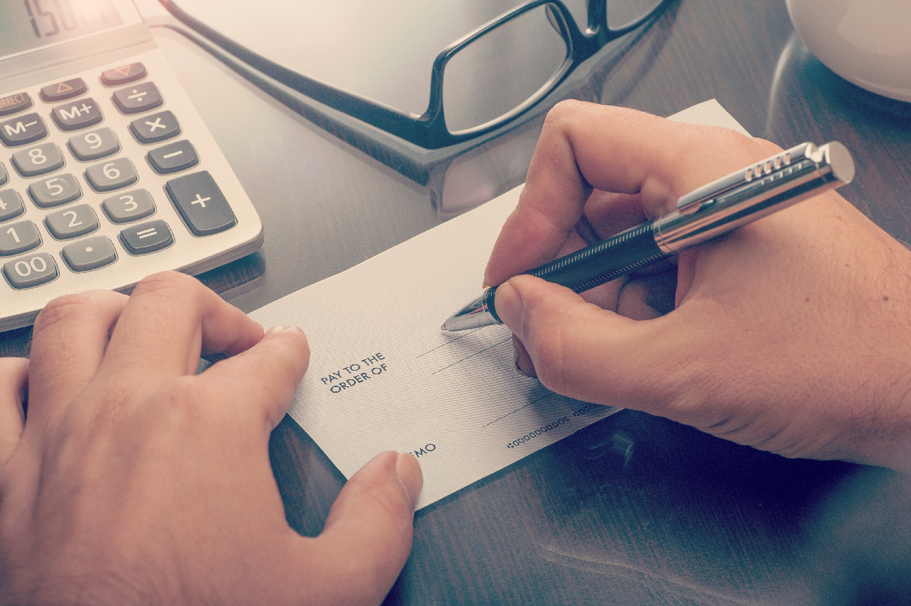 man writing a check on wooden desk